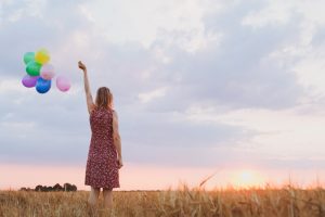 woman staring at the sun while holding colorful balloons