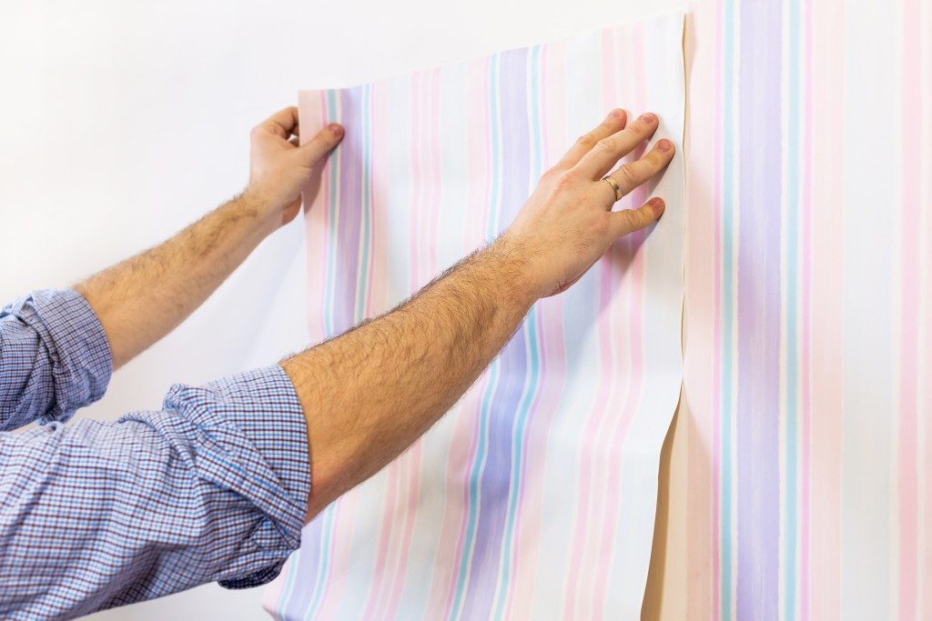 Handyman putting up wallpaper on the white walls