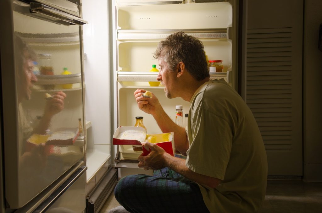 man binge eating in front of the refrigerator